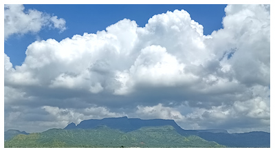 A photograph showing large fluffy clouds above hills. (Captured using phone)